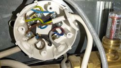 Otwarta puszka elektryczna z podłączonymi przewodami, obok element instalacji grzewczej z rotametrem