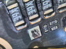 Mikroskopowe zbliżenie PCB z trzema elementami „2R2” i przypalonym układem SMD w kwadratowej obudowie.