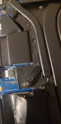 Zbliżenie na wnętrze laptopa, widoczne elementy chłodzenia i części płyty głównej ze śrubami.