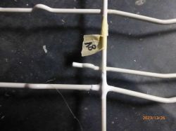 Zbliżenie na fragment kosza zmywarki z przyklejoną taśmą oznaczoną numerem „18”.