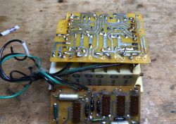 Two stacked PCBs with solder traces, components, and wires on a wooden workbench
