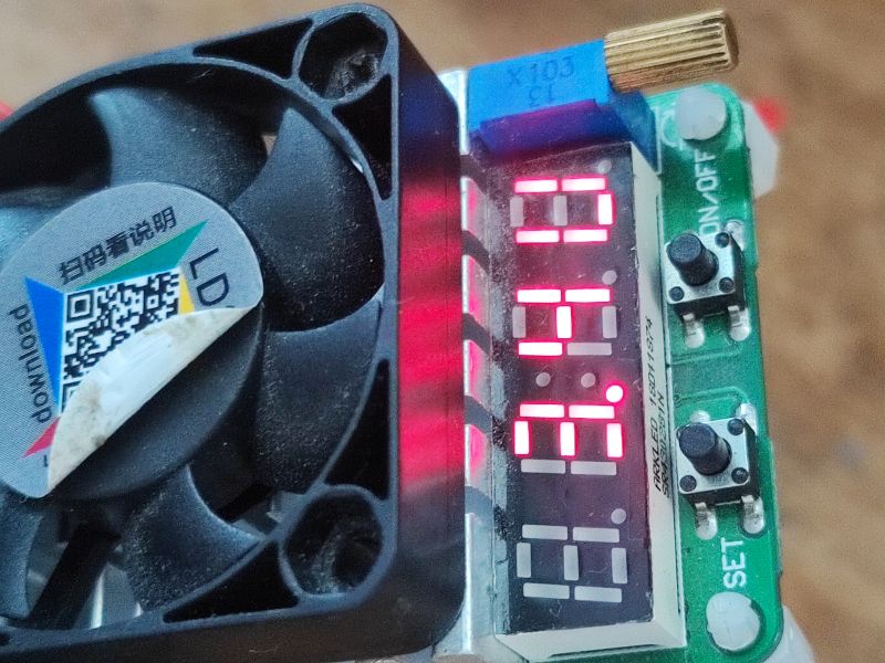 Zbliżenie na wentylator z naklejką QR oraz cyfrowy wyświetlacz z czerwonymi cyframi i przyciskami funkcyjnymi na płytce elektronicznej.