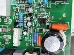 Fragment płytki drukowanej z różnymi elementami elektronicznymi, w tym kondensatorami, rezystorami i złączem, na zielonym tle PCB.