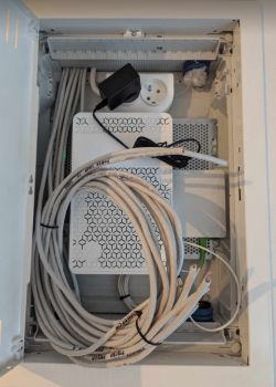 Zdjęcie skrzynki telekomunikacyjnej z routerem i kablami Ethernet.