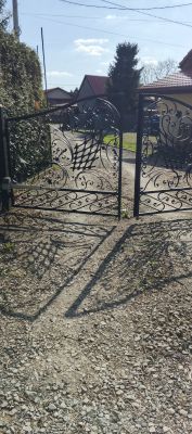 Otwarta metalowa brama wjazdowa z ozdobnymi wzorami na wiejskim podjeździe.