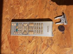 Pilot do telewizora marki Philips leżący na drewnianym stole obok pustej komory na baterie i baterii CR2025.