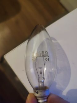Żarówka SOLEO 230V 60W trzymana w dłoni nad białym blatem
