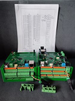 Dwa zielone moduły sterownika PLC typu EPIA z widocznymi złączami śrubowymi i elektroniką, ustawione przed wydrukowanym schematem elektrycznym.