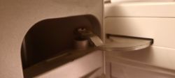 Widok wewnętrznej części obudowy drzwi chłodziarki, na której widać metalowy zawias bez plastikowej tulei.