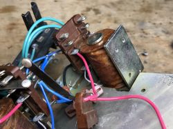 Close-up of a device interior with a relay coil, metal bracket, and colored wires on screw terminals