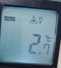 Wyświetlacz termometru bezdotykowego pokazujący temperaturę 2,7°C z ikonami HOLD, laseru i żarówki.