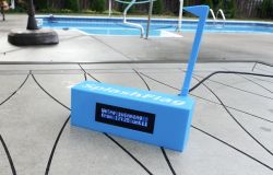 Niebieskie urządzenie SplashFlag z wyświetlaczem LCD ustawione przy basenie