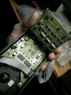 Wnętrze sterownika elektronicznego z widoczną rozbudowaną płytką PCB, licznymi układami scalonymi i przewodem taśmowym.