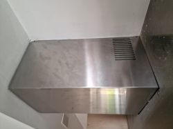 Górna metalowa osłona okapu kuchennego Samsung HC9247BX/XEO zamontowana ciasno między ścianami.