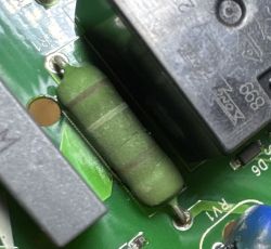 Zielony rezystor z paskami kolorowymi zamontowany na płytce PCB obok czarnego przekaźnika.