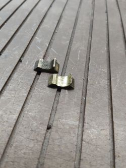Dwa metalowe półnakrętki leżące na rowkowanej powierzchni