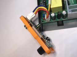 Panel czołowy elektronicznej stacji lutowniczej z pomarańczową ramką, odłączony od głównej płytki z przewodami i widocznymi podzespołami.