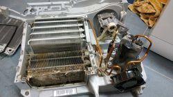 Disassembled dryer unit with dirty heat exchanger, copper pipes, compressor, and fan inside a plastic housing