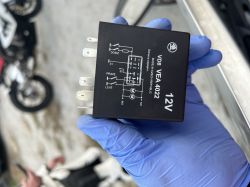 Osoba w niebieskiej rękawiczce trzyma przekaźnik samochodowy o oznaczeniu VD8 VEA 4022 12V firmy Škoda.