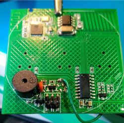 Close-up of a green PCB from a wall switch with an added buzzer and an extra wire soldered.