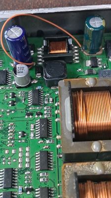 Zbliżenie płytki PCB z cewkami, kondensatorami i cienkim pomarańczowym przewodem mostkującym