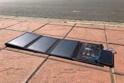 Foldable solar panel on sidewalk with smartphone connected via USB cable