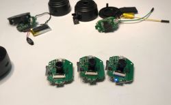 Three disassembled camera modules with visible PCBs and lenses, along with housing parts and batteries on a white surface.