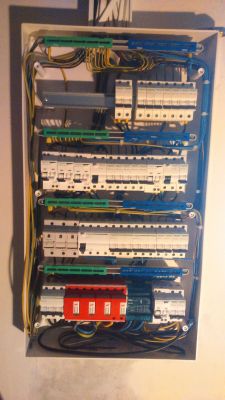 Widok na tablicę elektryczną z różnymi zabezpieczeniami i przewodami.