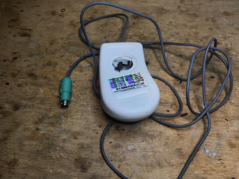 Old PS/2 Ball Mouse Old ball mouse with a cable ending in a PS/2 plug, lying on a wooden table.