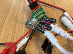 Connecting Debugging Wires to CB3S/BK7231N LED Controller CB3S/BK7231N module with attached debugging wires and pogo connector, placed on a wooden surface.