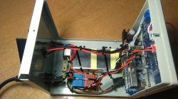 Wnętrze otwartego zasilacza z widocznymi przewodami i elementami elektronicznymi.
