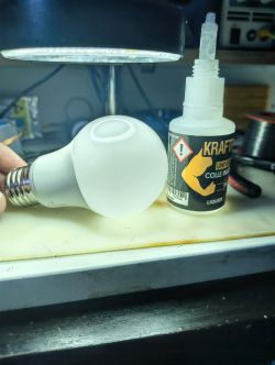 LED light bulb on a work surface next to a “KRAFT” glue bottle, tools in the background