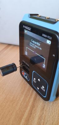 Miernik F-NIRSI DSO-TC3 testujący kondensator elektrolityczny 680µF na drewnianej powierzchni.