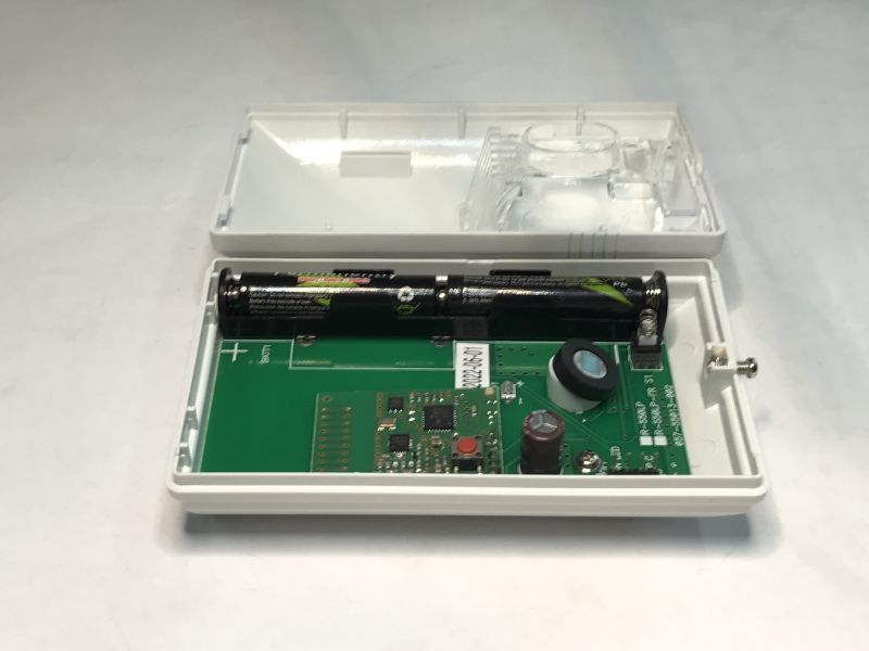 An open plastic case with a visible circuit board, two AA batteries, and electronic components inside.