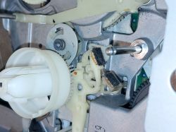 Zbliżenie na mechanizm wewnętrzny urządzenia z elementami plastikowymi i metalowymi, widoczne kawałki filcu.