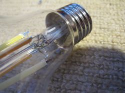Close-up of an LED light bulb lying on a beige carpet, showing the screw base and internal components.