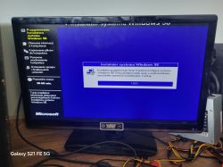 Monitor pokazujący proces instalacji systemu Windows 98 z widocznym paskiem postępu na 100%.