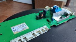 Zbliżenie na zieloną płytkę drukowaną z widocznymi elementami elektronicznymi, takimi jak kondensatory, rezystory, cewka i złącza.