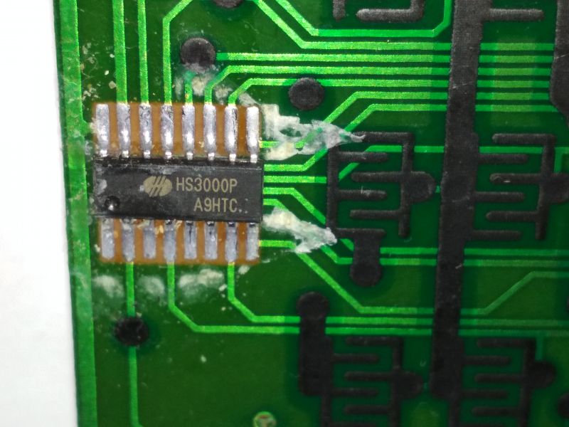 Zbliżenie na układ scalony na płytce drukowanej z oznaczeniami HS3000P A9HTC, otoczony zanieczyszczeniami.
