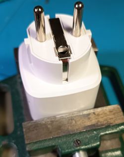 White Type E power plug with two round pins and a metal grounding contact, held in a vise