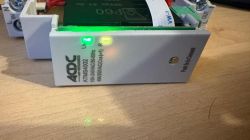 Close-up of an ACDC ATM5A002 relay module with green and yellow LEDs on a wooden surface.