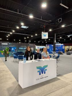 Trade fair booth with a white counter showing the VF logo and three people standing behind it in an expo hall.