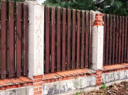Drewniany płot na murowanej podmurówce z uszkodzonymi, kruszącymi się słupkami