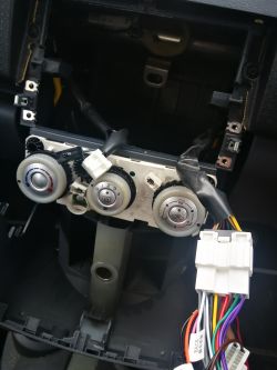 Wewnątrz deski rozdzielczej Mitsubishi Colt 2007 z odkrytym panelem klimatyzacji i przewodami do radia.