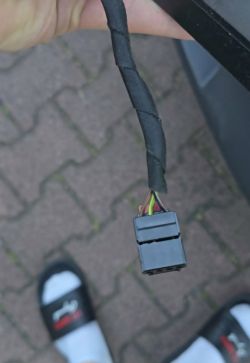 Grauer Elektrostecker an einem mit schwarzem Band umwickelten Kabelstrang, in der Hand im Freien gehalten.