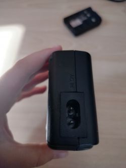 Osoba trzymająca czarną ładowarkę z widocznym gniazdem oznaczonym jako AC IN.