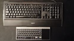 Dwie klawiatury na ciemnym tle: duża Logitech k740 i mniejsza bezprzewodowa klawiatura z touchpadem.