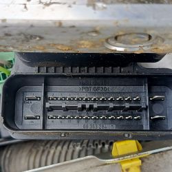 Zbliżenie na złącze elektryczne samochodowego sterownika ABS z widocznymi numerami pinów.
