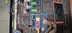 Electronics test setup with circuit boards, wiring, and three color displays showing spectrum/VU meters
