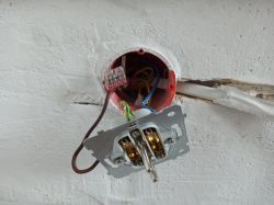 Zbliżenie na instalację elektryczną ze ściany z widocznymi przewodami i gniazdkiem.